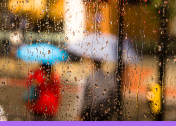 Rain falling on a window with people holding umbrellas blurred through the window. 